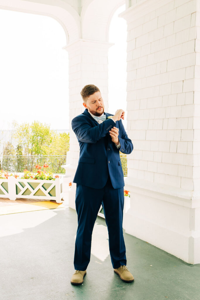 Man adjusting cuff links before wedding on white hotel porch on Mackinac Island