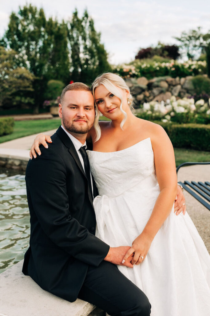 newly married couple sitting on stone wall in front of garden