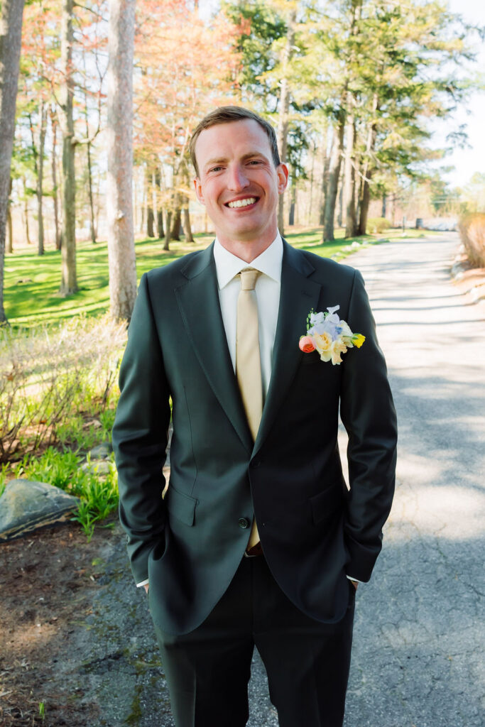 man wearing black tux posing in front of trees