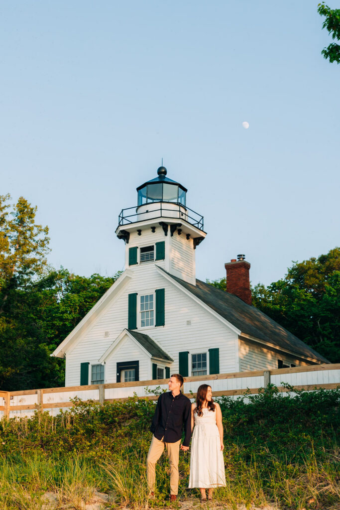 Man and woman standing holding hands in front of Old Mission Lighthouse in Traverse City